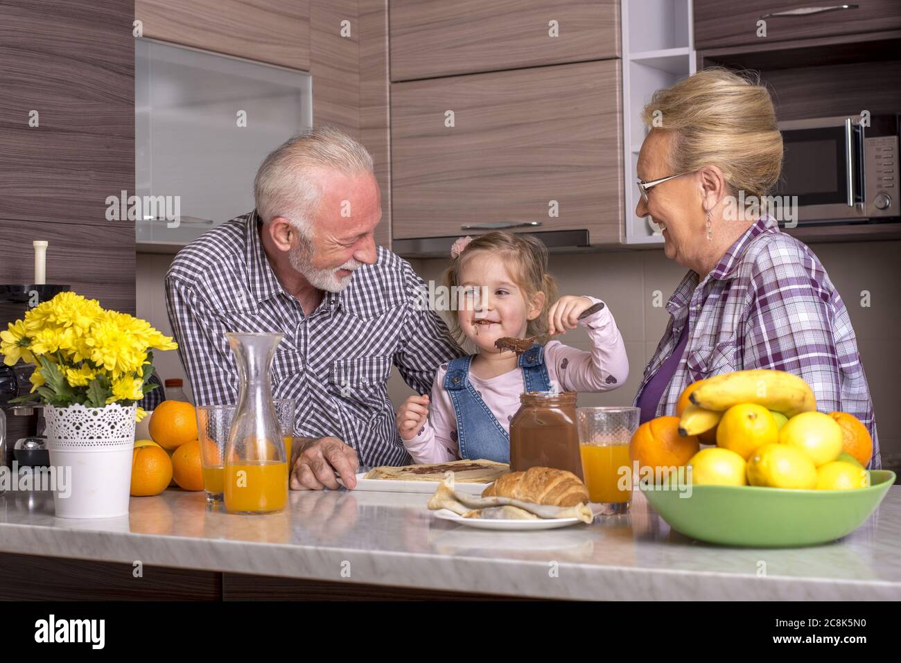 Grandparents and granddaughter preparing pancakes with chocolate cream in the kitchen Stock Photo
