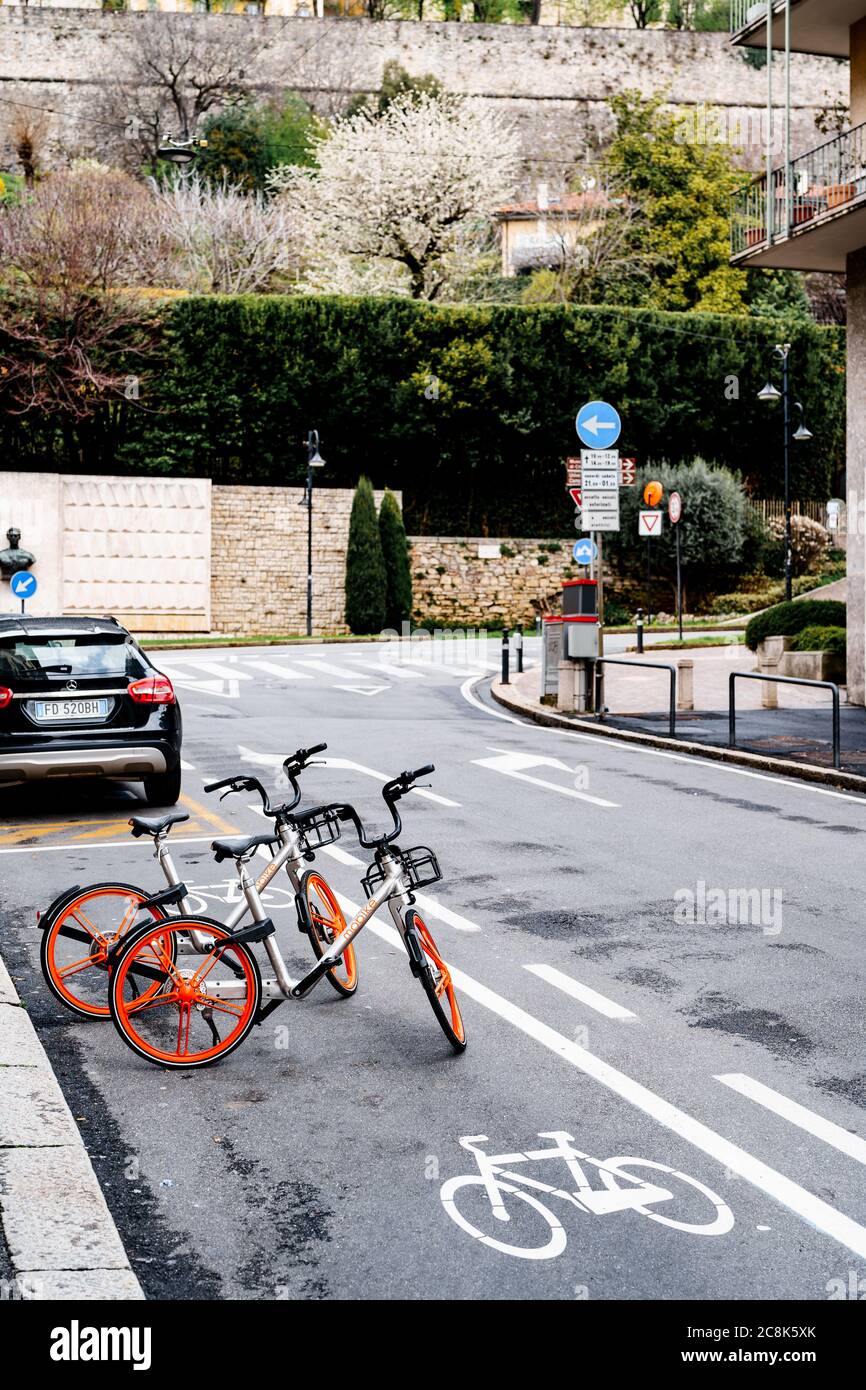 Bicycle parking in the middle of the road by green spaces and a brick fence Stock Photo