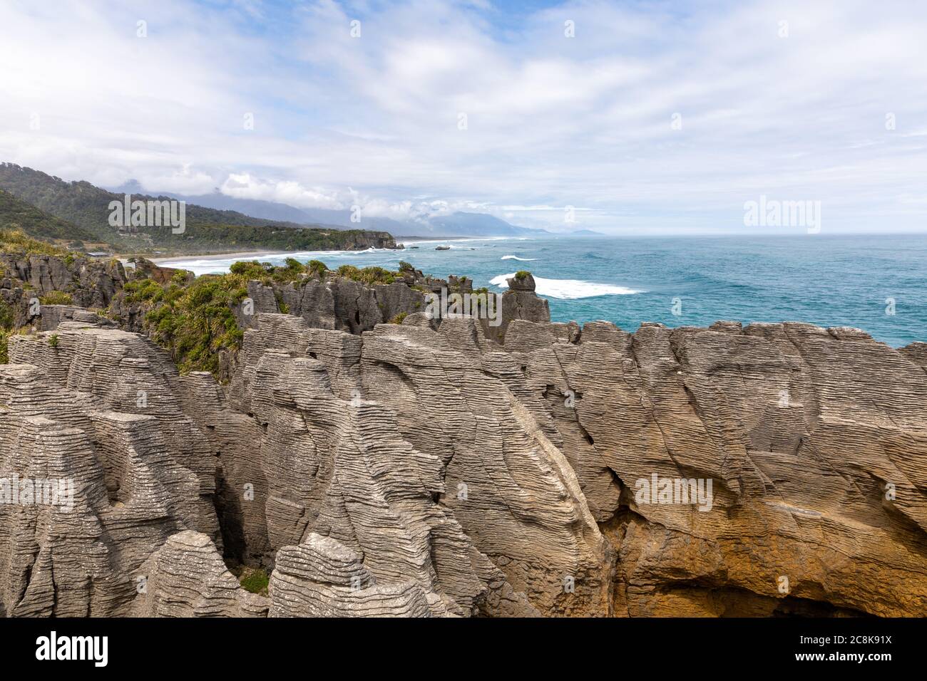 The famous Pancake Rocks on Dolomite Point with a view out over the sea towards mountains covered in clouds. Dolomite Point, South Island, New Zealand Stock Photo