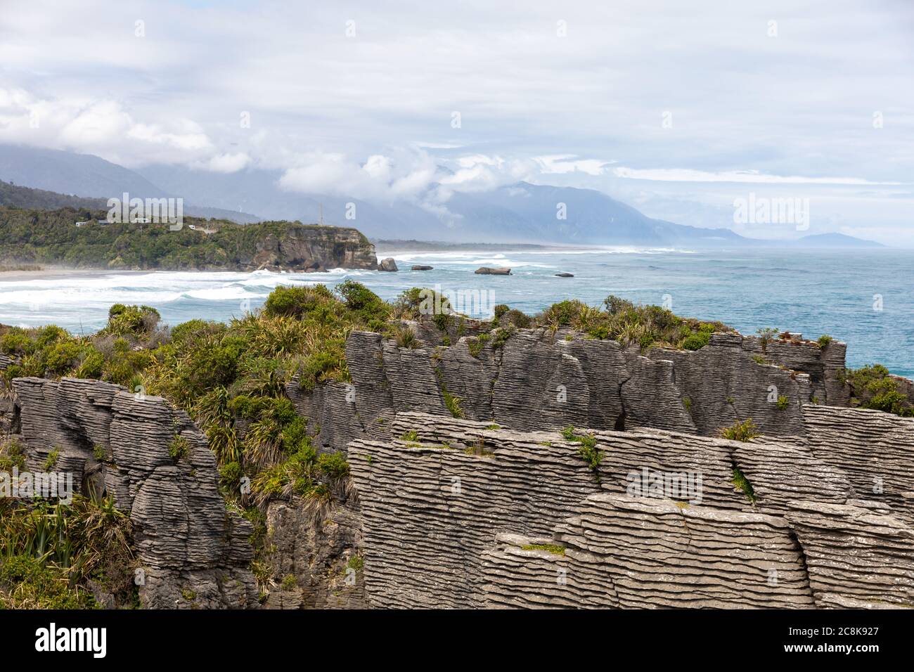 The famous Pancake Rocks on Dolomite Point with a view out over the sea towards mountains covered in clouds. Dolomite Point, South Island, New Zealand Stock Photo