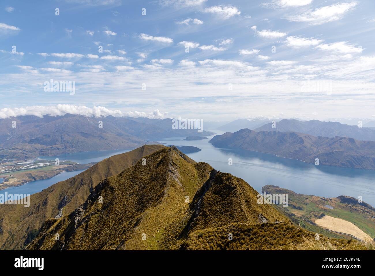 The view from Roys Peak Lookout over a ridge with Lake Wanaka and white pattered clouds on a blue sky. Stock Photo