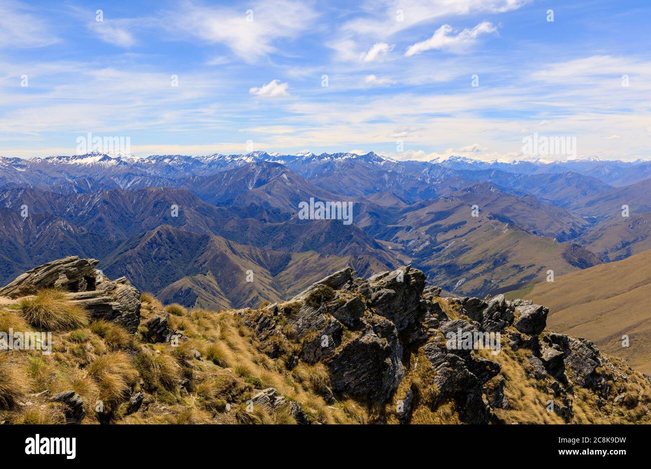 View of the Southern Alps from the climb up Ben Lomond. Tussocks and rocks in the foreground and snow-capped mountains in the background. Stock Photo