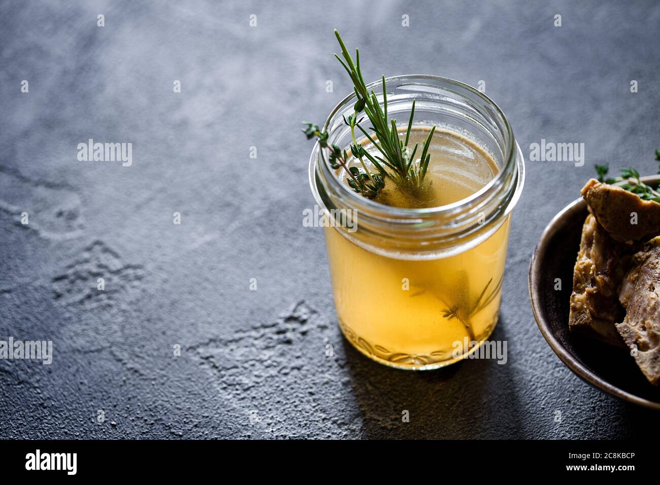Glass jar with yellow fresh bone broth on dark gray background. Healthy