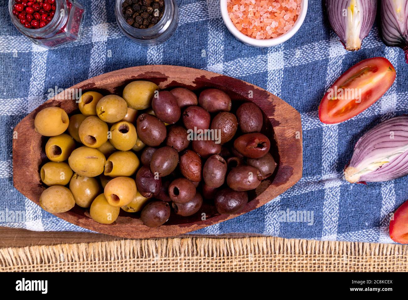 Portion of black, green olives, bowl with pink himalayan salt and glass jars with grains of red and black pepper. Stock Photo