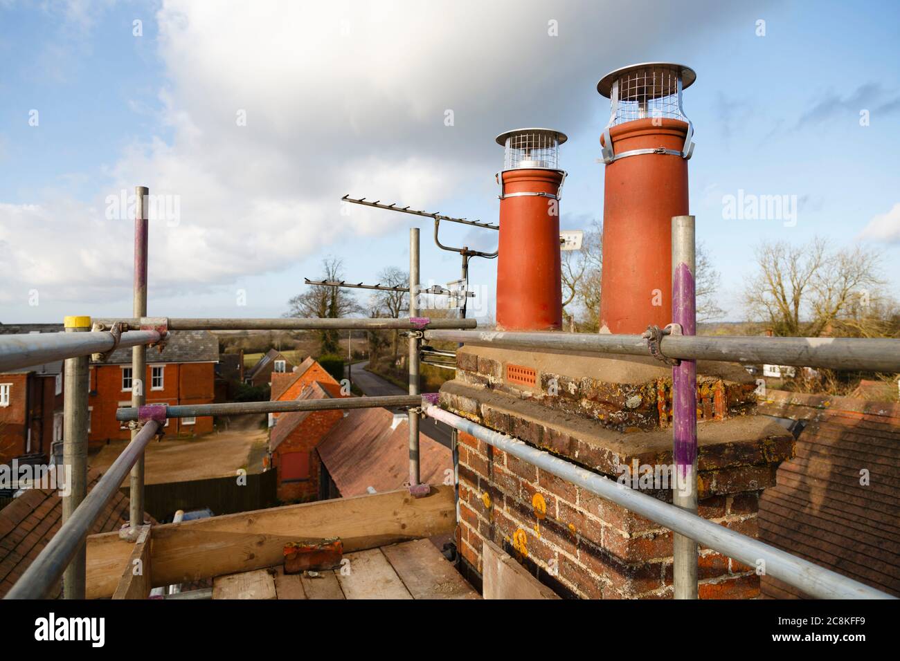 Repairing chimney pots with scaffolding on a roof. Construction work on a house renovation, UK Stock Photo