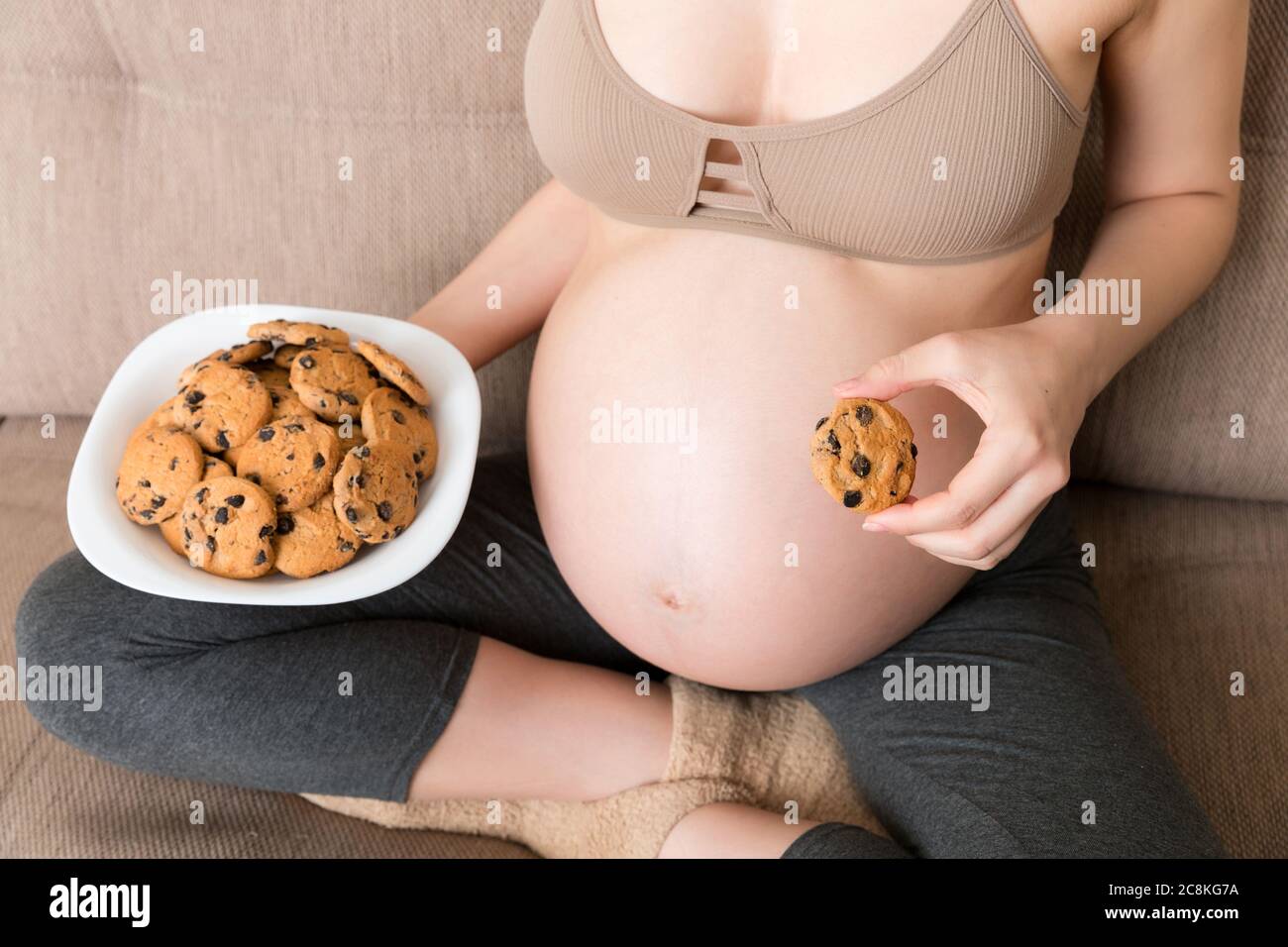 Close up of pregnant woman enjoys eating cookies resting on the sofa at