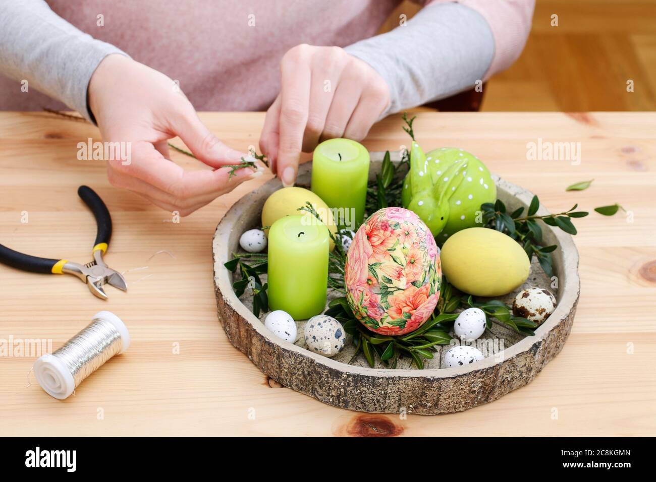 Florist at work: woman arranges an Easter table decoration with eggs, candles and ceramic figurines. Step by step, tutorial. Stock Photo
