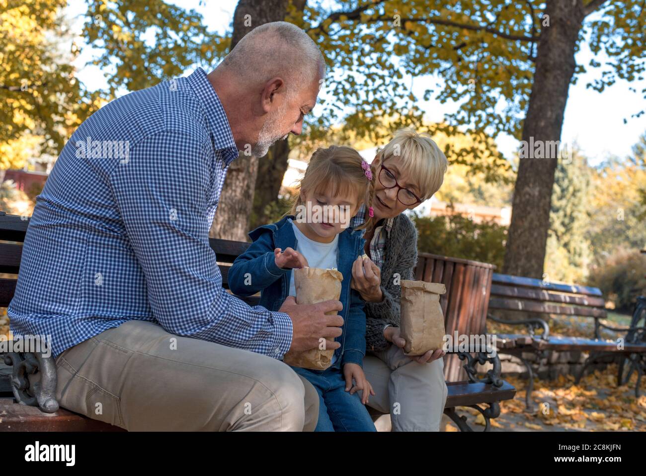 Beautiful picture of grandparents eating popcorn with their grandchild in the park Stock Photo