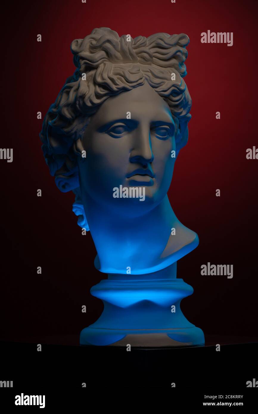 Plaster statue of a bust of Apollo Belvedere in blue local light on a red background Stock Photo