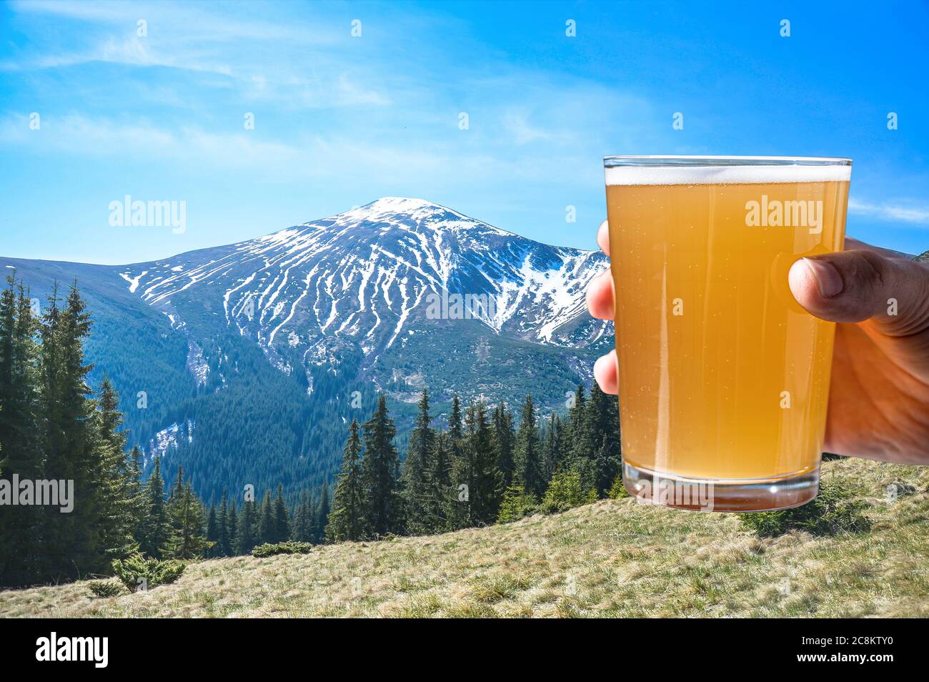 Man holding glass of light beer with view of mountains in Ukraine. Beautiful view of rocks, forest and blue sky in Carpathian Mountains in Ukraine. Stock Photo