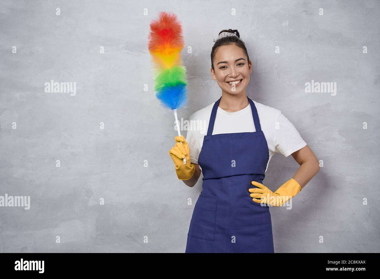 https://c8.alamy.com/comp/2C8KXAX/housekeeping-and-cleaning-service-concept-happy-young-woman-cleaning-lady-in-uniform-holding-colorful-microfiber-duster-and-smiling-at-camera-while-standing-against-grey-wall-2C8KXAX.jpg