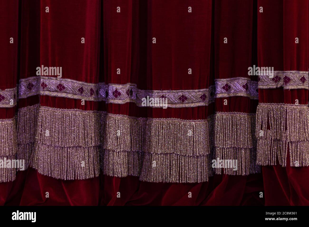 Theatrical dark red velvet curtain with golden fringe. Texture
