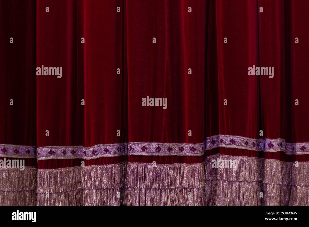Theatrical dark red velvet curtain with golden fringe. Texture ...