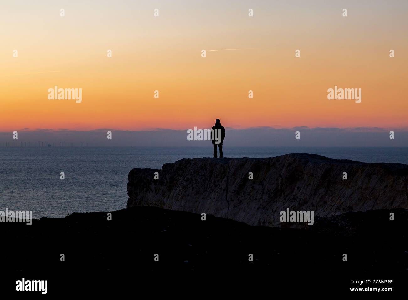 A silhouetted man standing on a cliff looking at the sunset over the ...