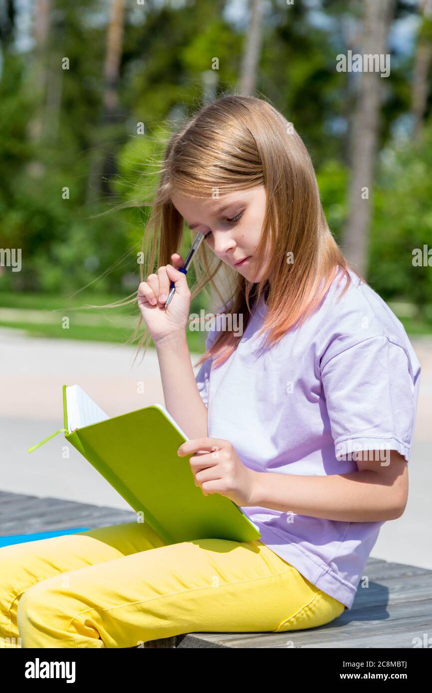 school girl sitting on bench in public park and making notes to her ...