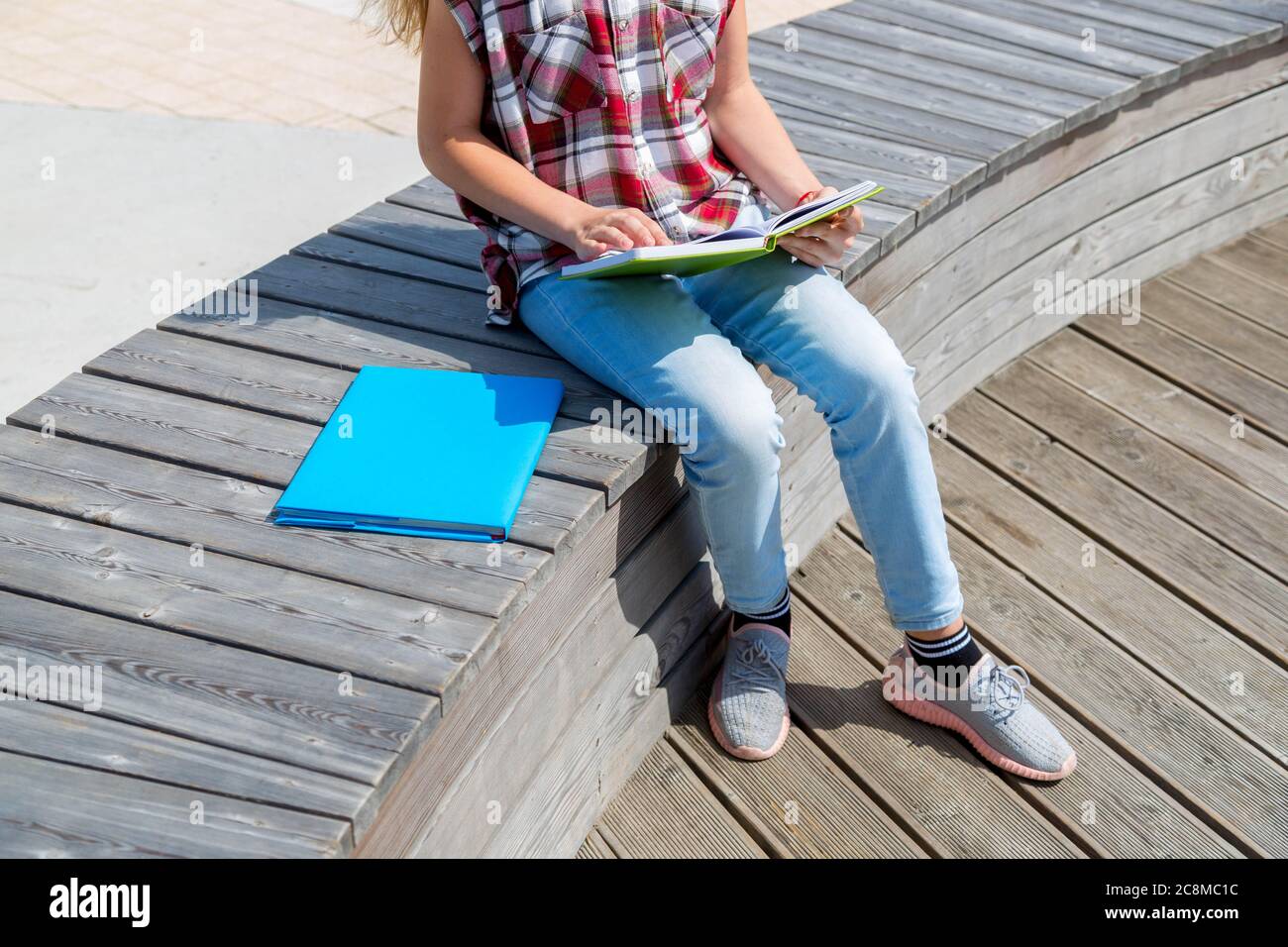 school girl sitting on bench in public park and making notes to her ...