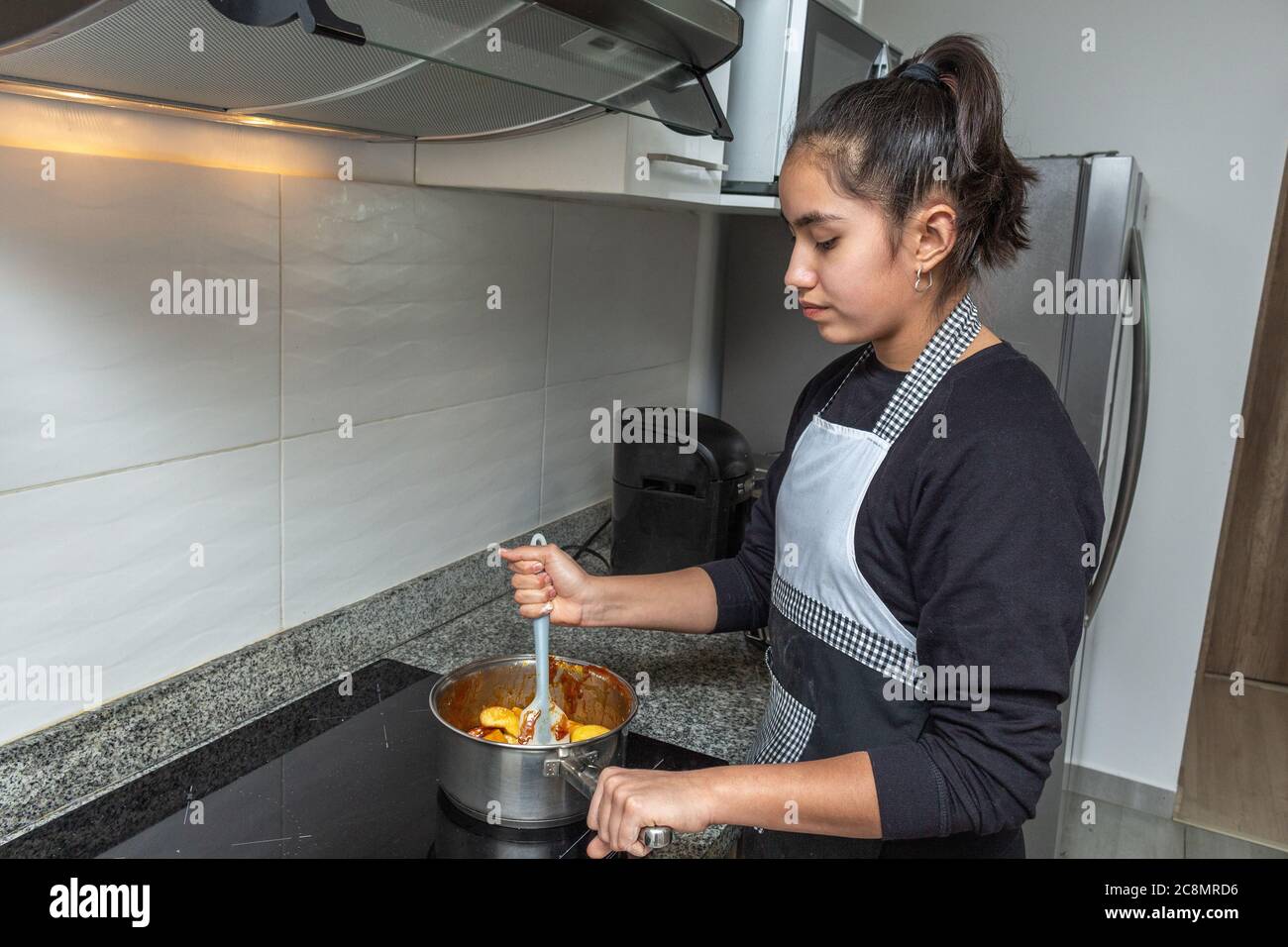 Teenage girl cooking apples with caramel to make a cake in her kitchen Stock Photo