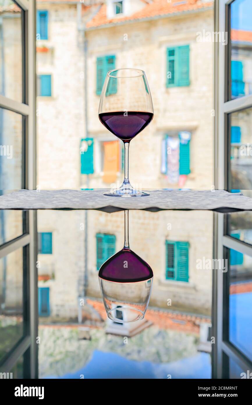 https://c8.alamy.com/comp/2C8MRNT/glass-or-red-wine-with-reflection-and-a-blurred-view-of-stone-houses-and-mountains-through-an-open-window-in-old-town-kotor-montenegro-2C8MRNT.jpg