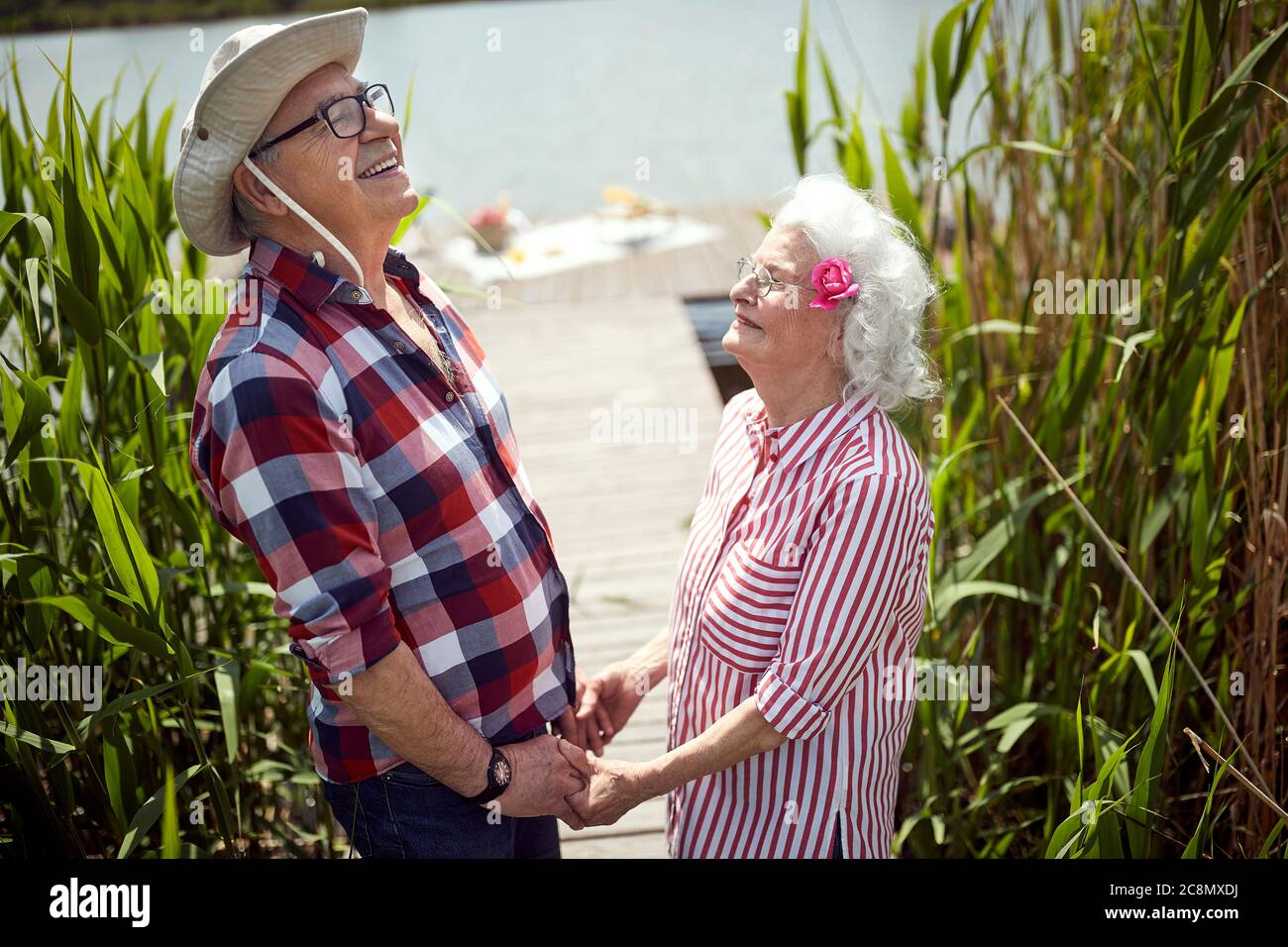 close up of cute caucasian senior couple holding hands, looking up, laughing,  standing by the river Stock Photo