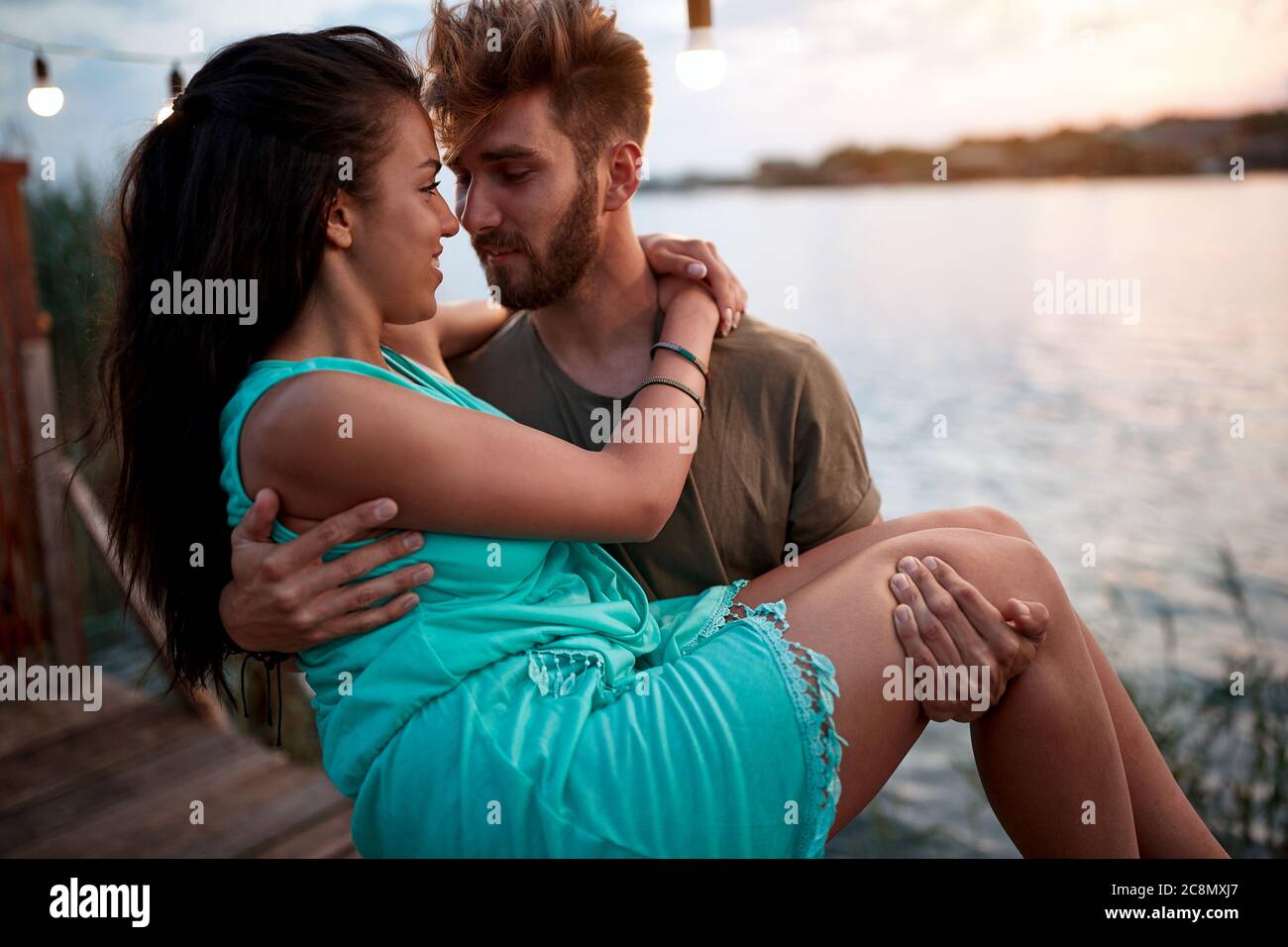 young beardy man holding in arms beautiful woman, by the sea at sunset. romantic couple in love Stock Photo