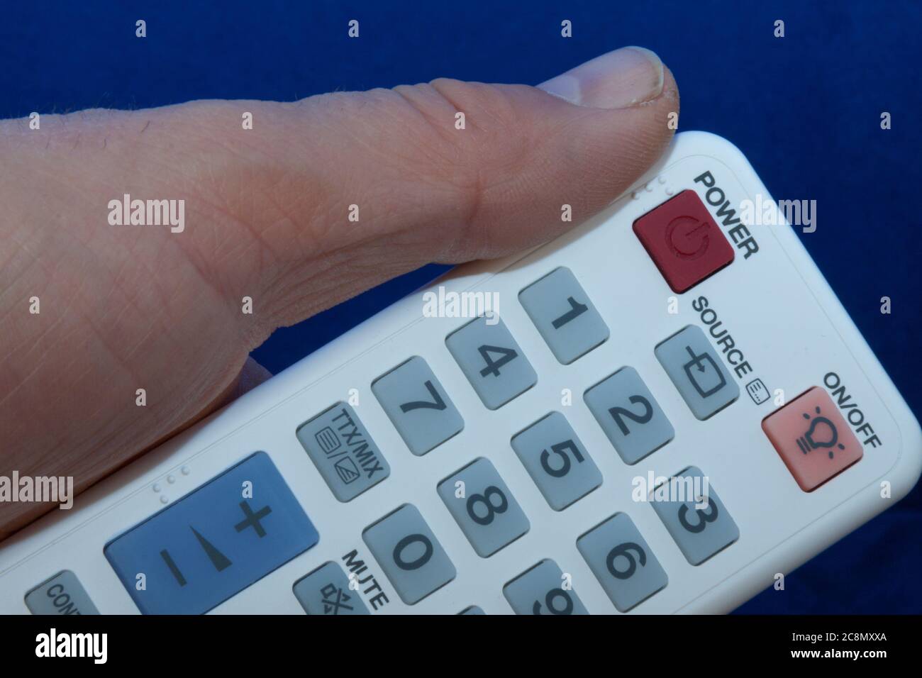 hand with a white remote control with multi-colored buttons Stock Photo