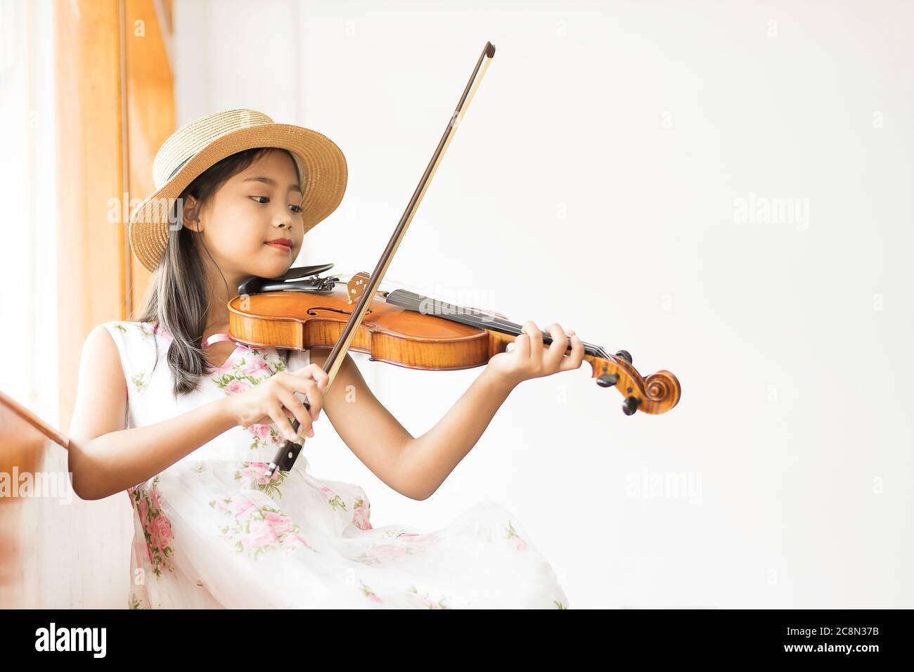 A cute Asian elementary school girl is playing a violin happily in her ...