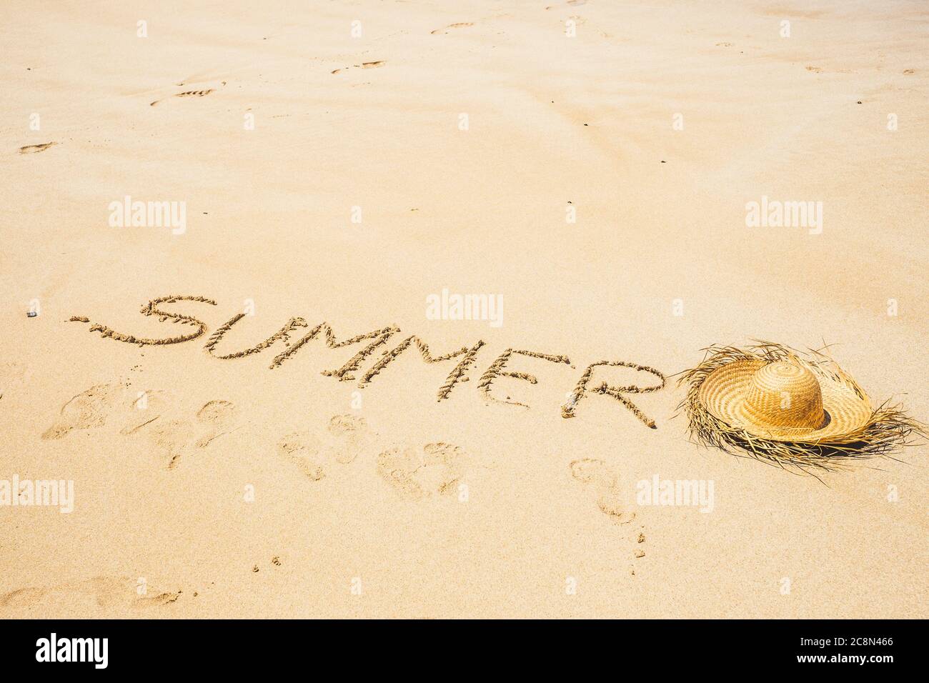 Summer holiday vacation at the beach concept for tourist and tourism - words wrote on the sand at the beach and sun hat on the ground - footprints aro Stock Photo
