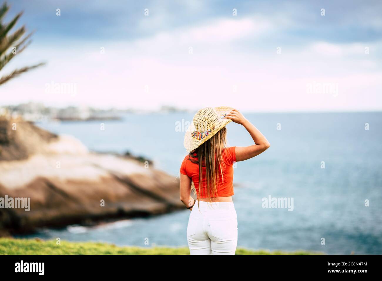 Tourism concept with beautiful female tourist viewed from back looking and enjoying the blue ocean and sky - summer holiday vacation and outdoor leisu Stock Photo