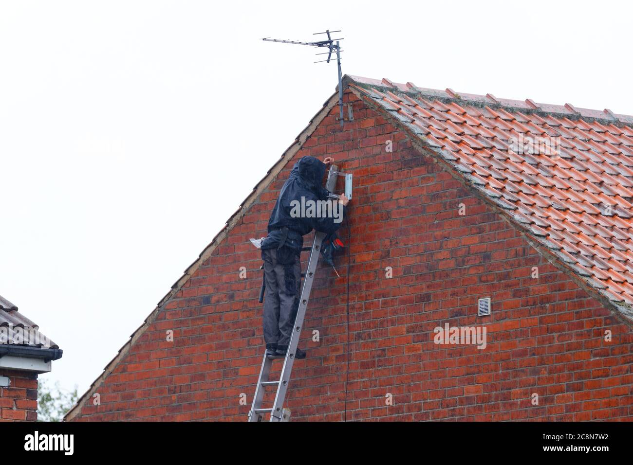 A man installing a tv aerial on a house, while it's raining Stock Photo Alamy