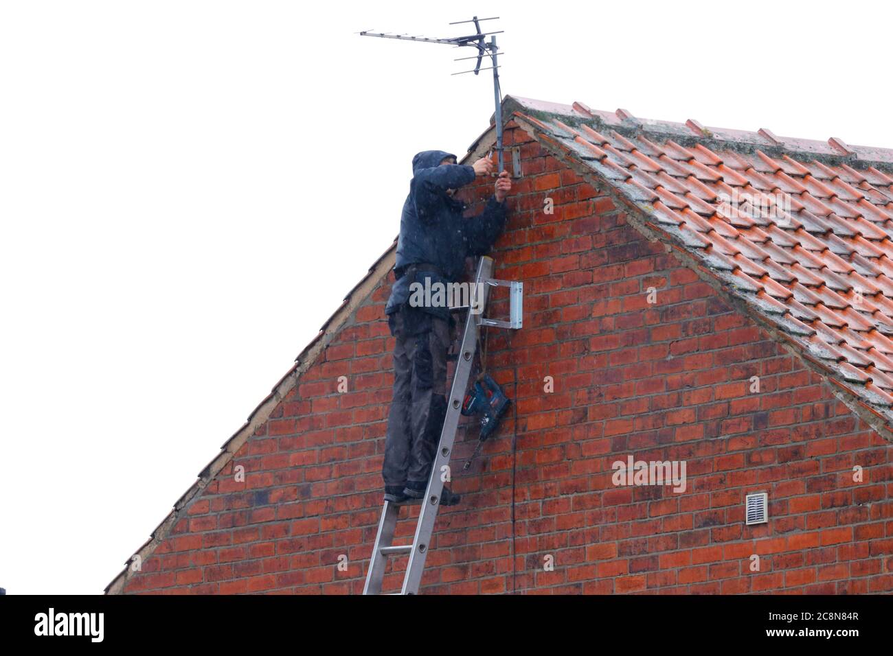 A man installing a tv aerial on a house, while it's raining Stock Photo Alamy