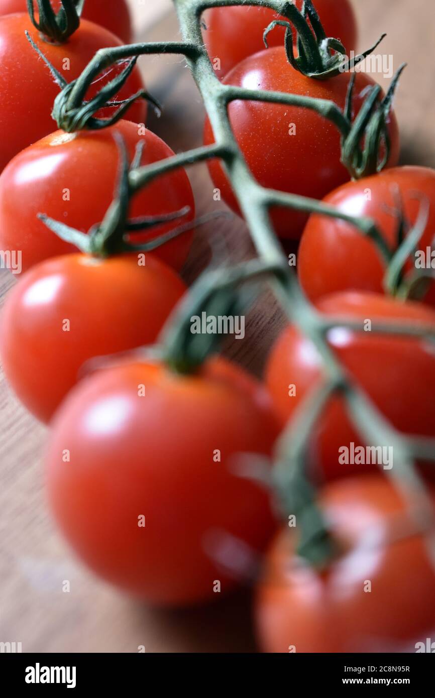 Red cherry tomatoes on the vine, close up on a wooden chopping board under natural light. Stock Photo