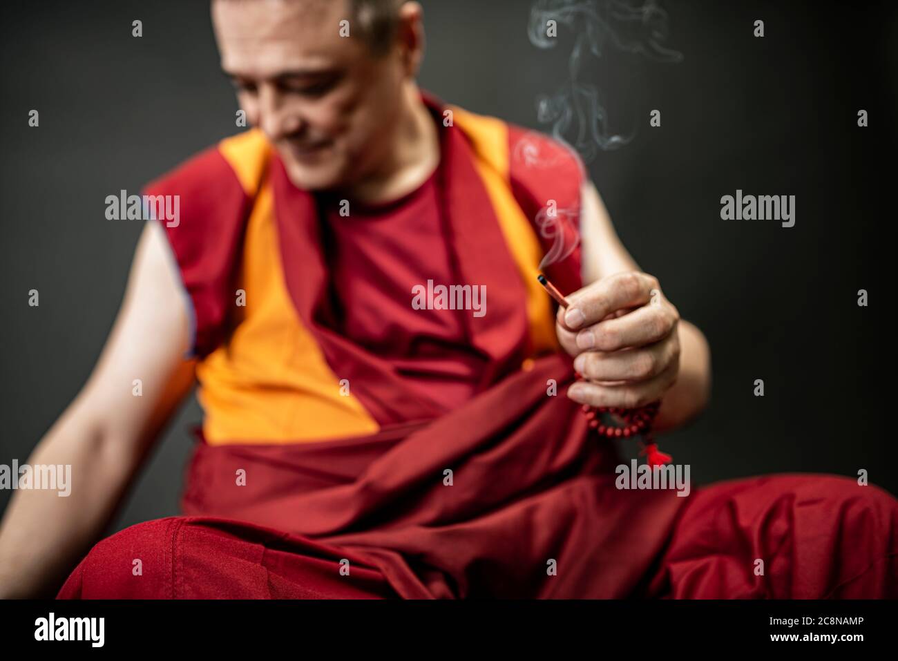 Buddhist monk in red kesa, holding an incense stick with incense in his ...