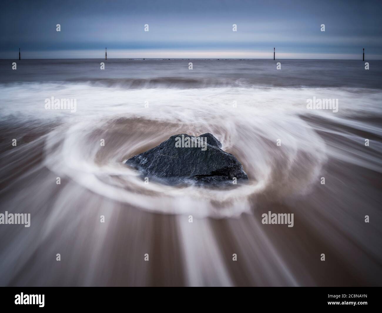 Receeding waves making a circular pattern aound a lone rock on Sea Palling beach. Stock Photo