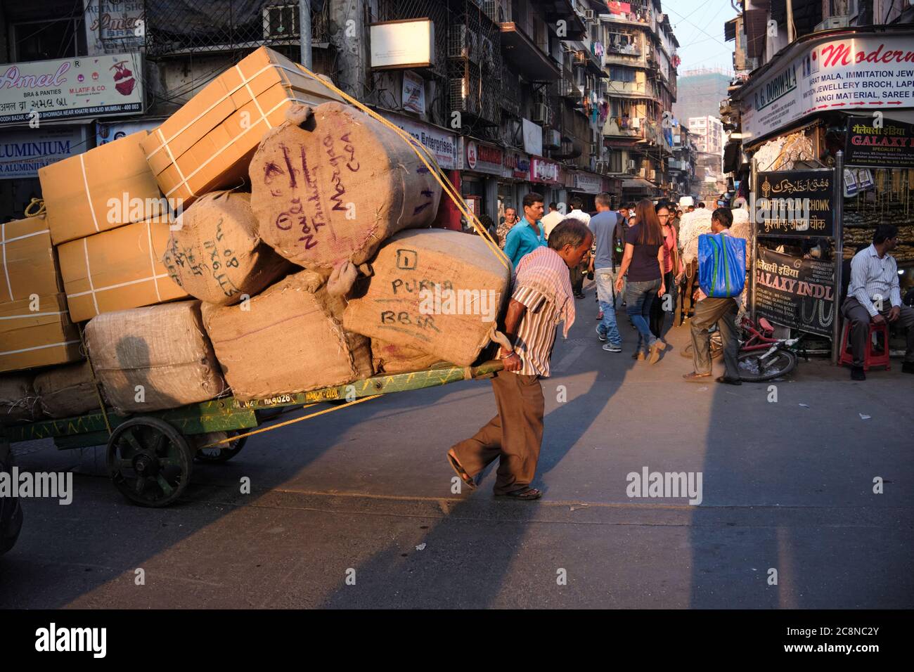 A man pulls a heavy handcart through Kalbadevi Rd. in Bhuleshwar, Mumbai, India, handcarts being the most used mode for goods transport in the area Stock Photo
