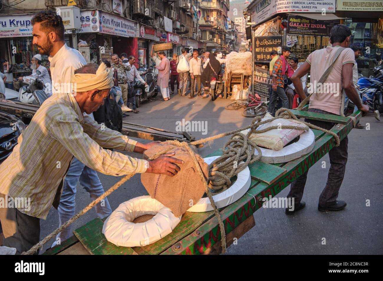 Two men steer a handcart through busy Kalbadevi Rd. in Bhuleshwar, Mumbai, India, handcarts being the most used mode for goods transport in the area Stock Photo