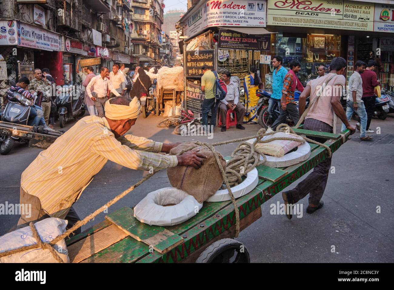 Two men steer a handcart through busy Kalbadevi Rd. in Bhuleshwar, Mumbai, India, handcarts being the most used mode for goods transport in the area Stock Photo