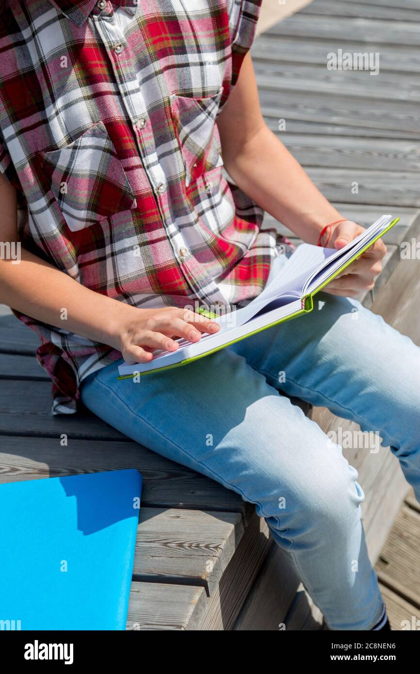 school girl sitting on bench in public park and making notes to her ...
