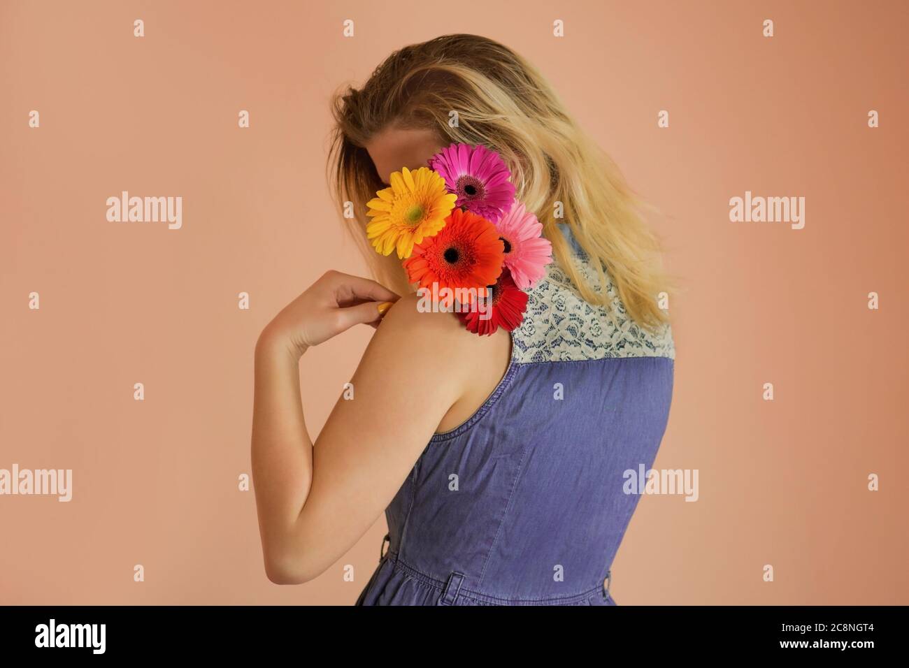 Cheerful young lady wearing denim dress and flowers chamomile in hands Stock Photo
