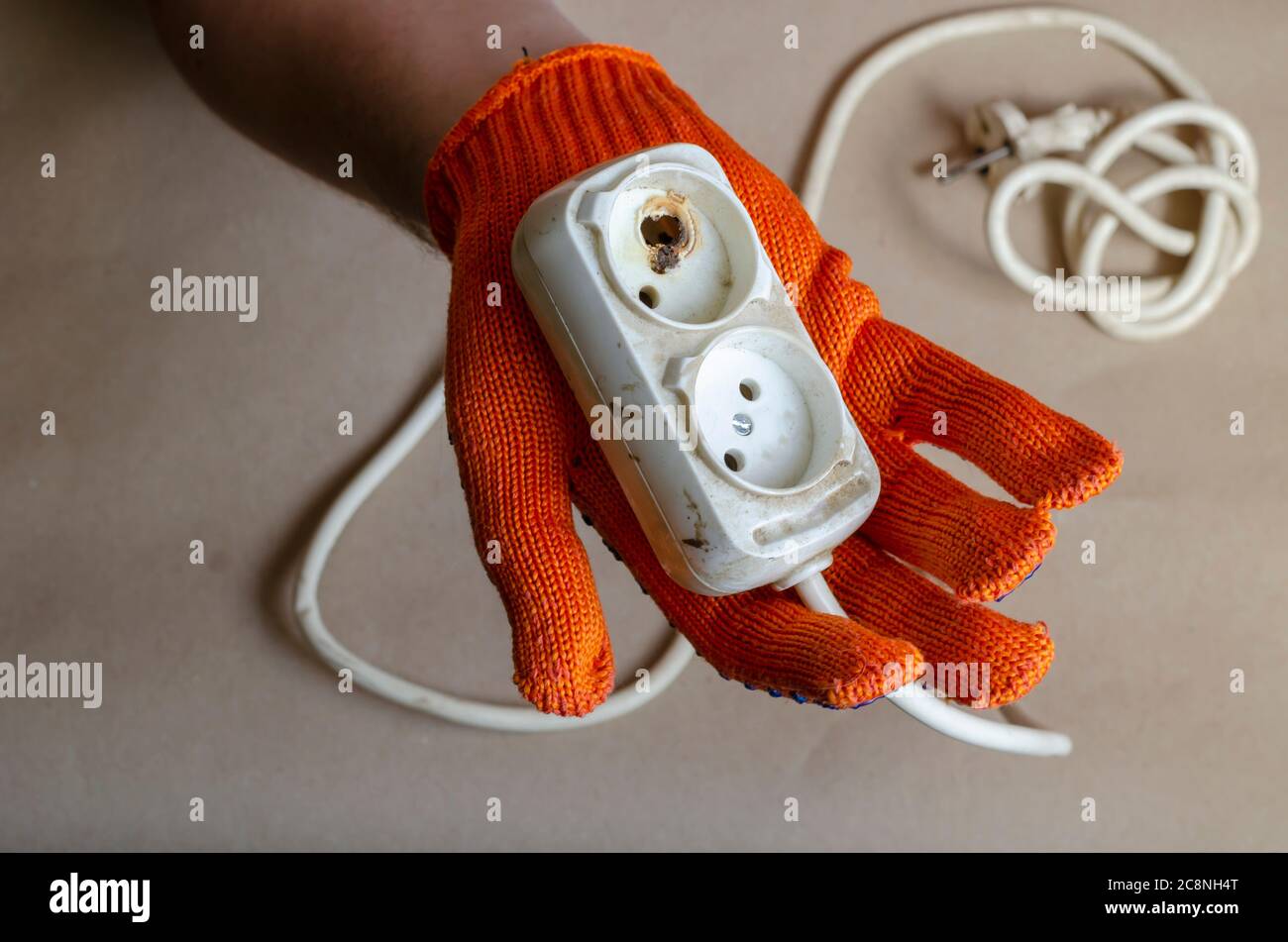 Hand wearing a protective orange glove holds an electrical outlet after