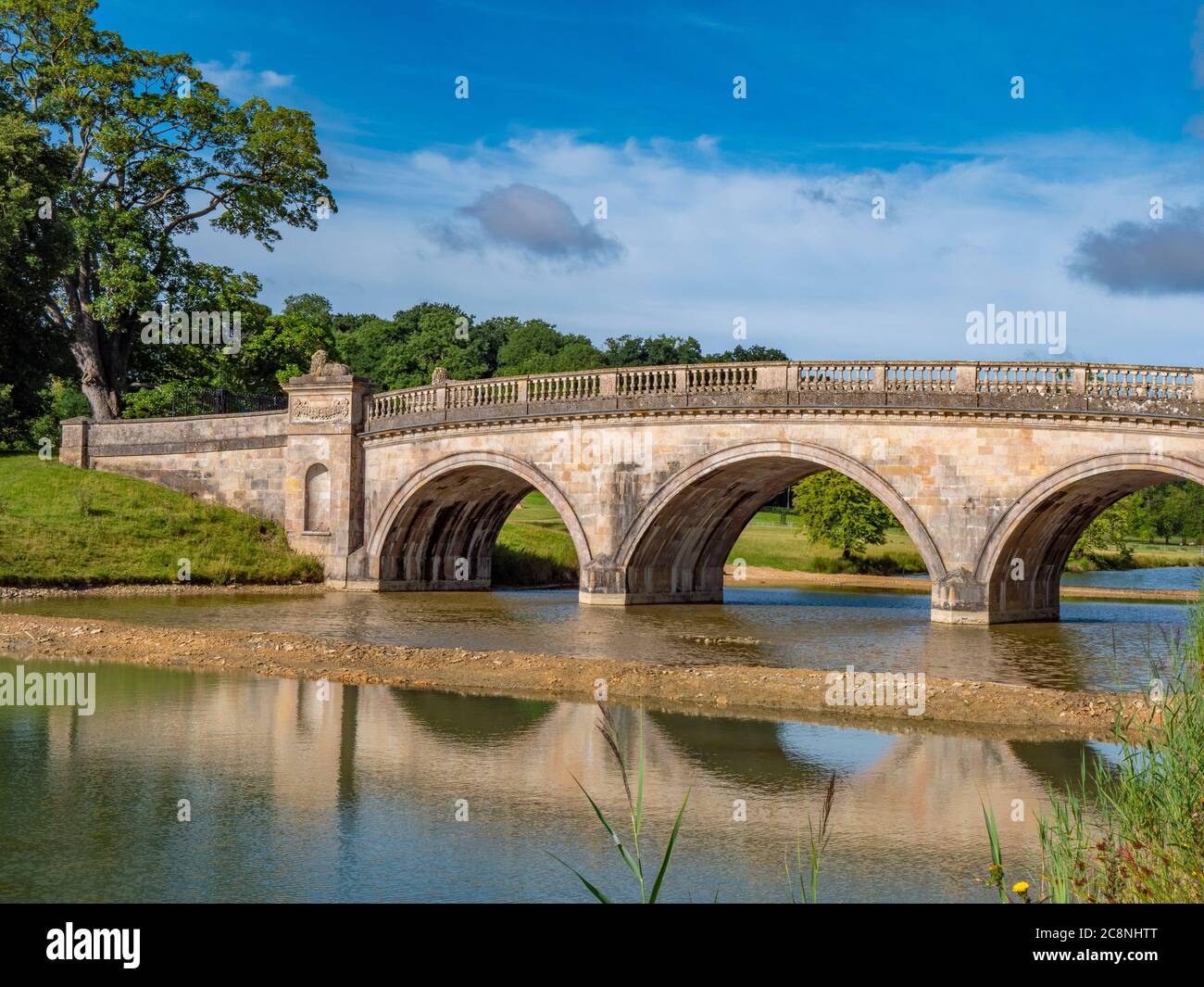 Lion Bridge - an 18th century, stone built crossing over the still lake on the Burghley House estate. Stamford, Lincolnshire, England, UK. Stock Photo