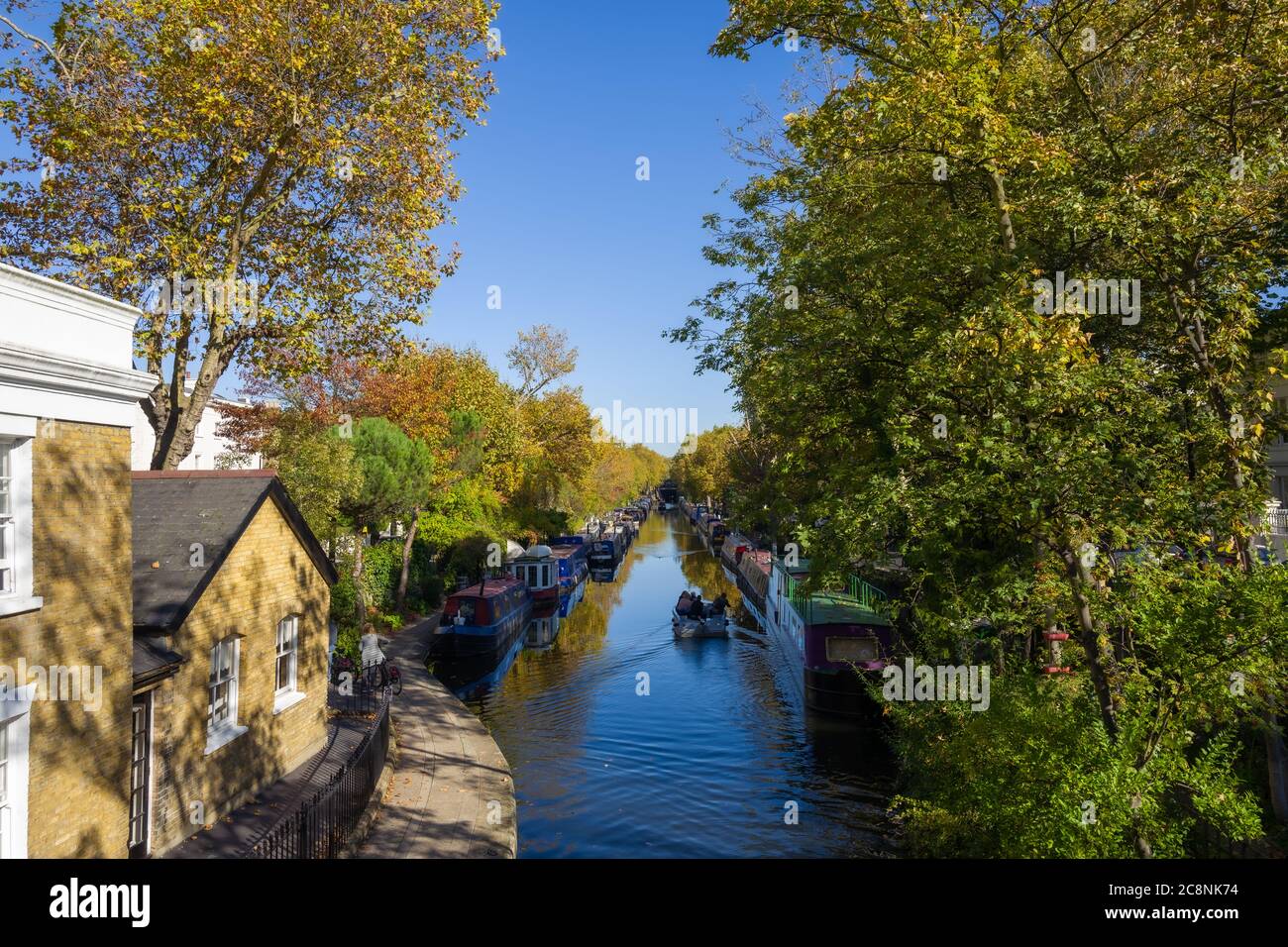 A view from the bridge down the canal at Little Venice. Shows trees, houseboats, towpath and boat ride on beautiful sunny autumn day. Stock Photo