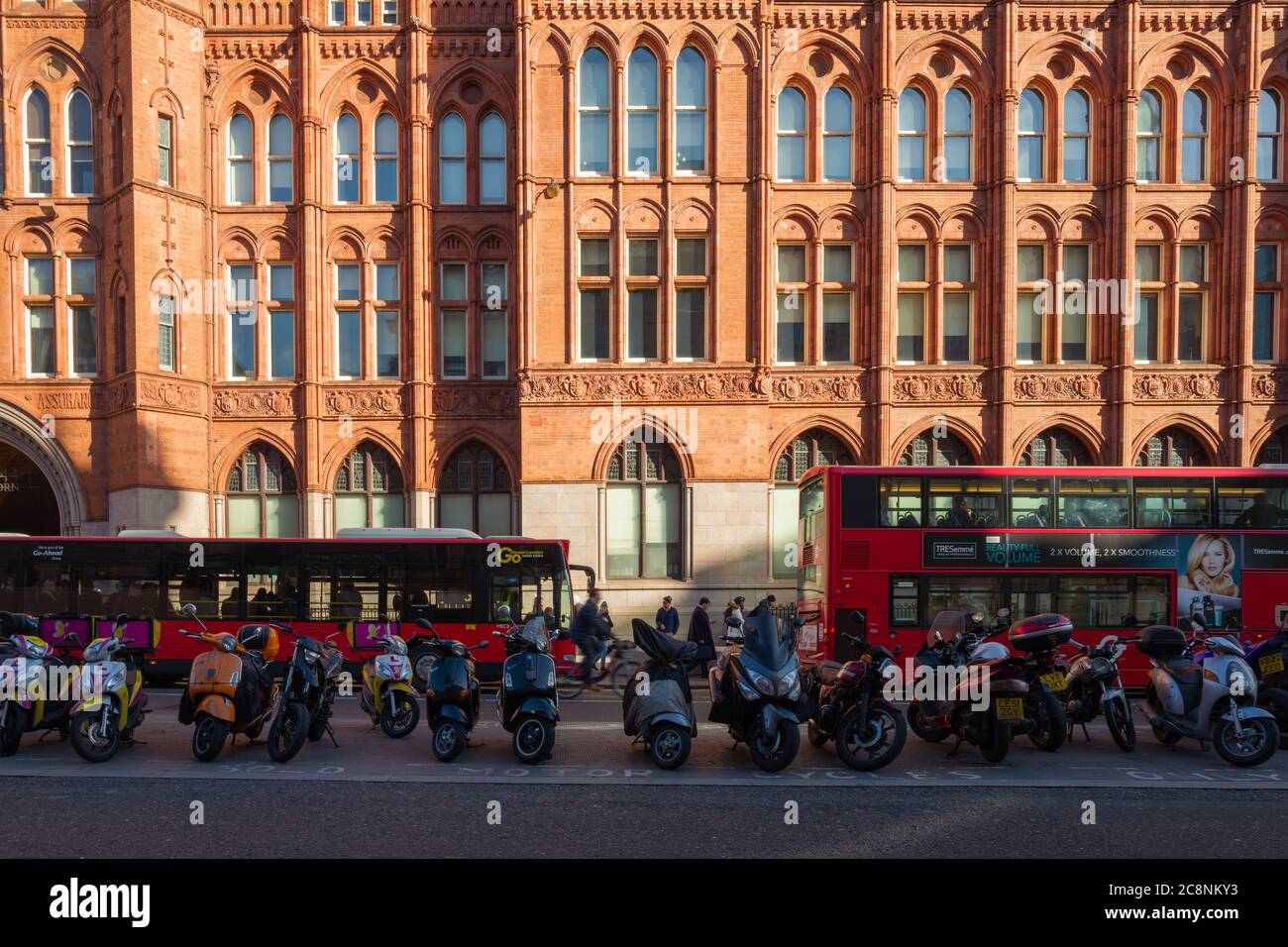 Parked motorbikes and red Transport for London buses in front of imposing terracotta facade of Prudential Assurance Building (aka Holborn Bars). Stock Photo