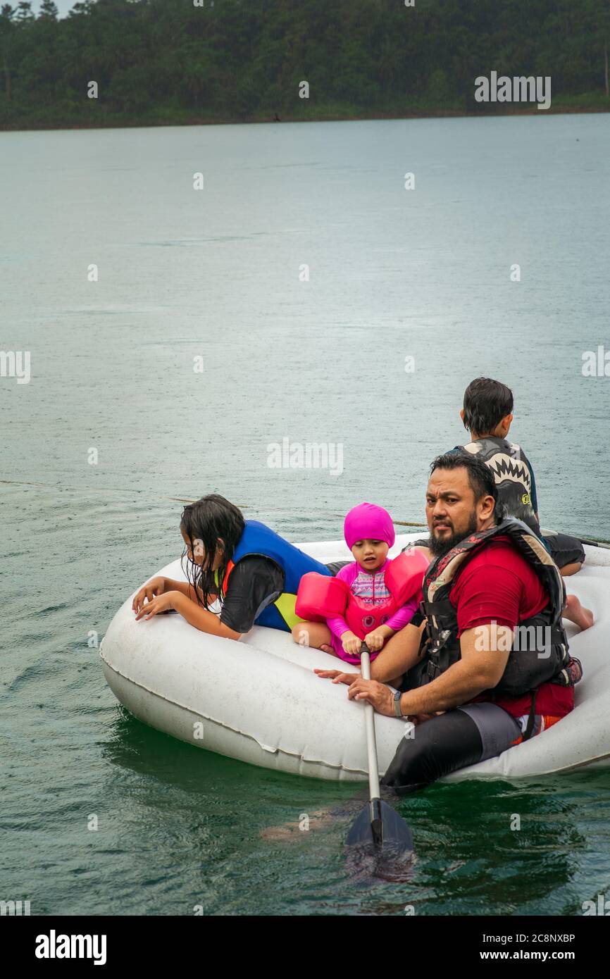 Family wearing life jackets paddling on an inflatable boat in Kenyir Lake, Malaysia. Stock Photo