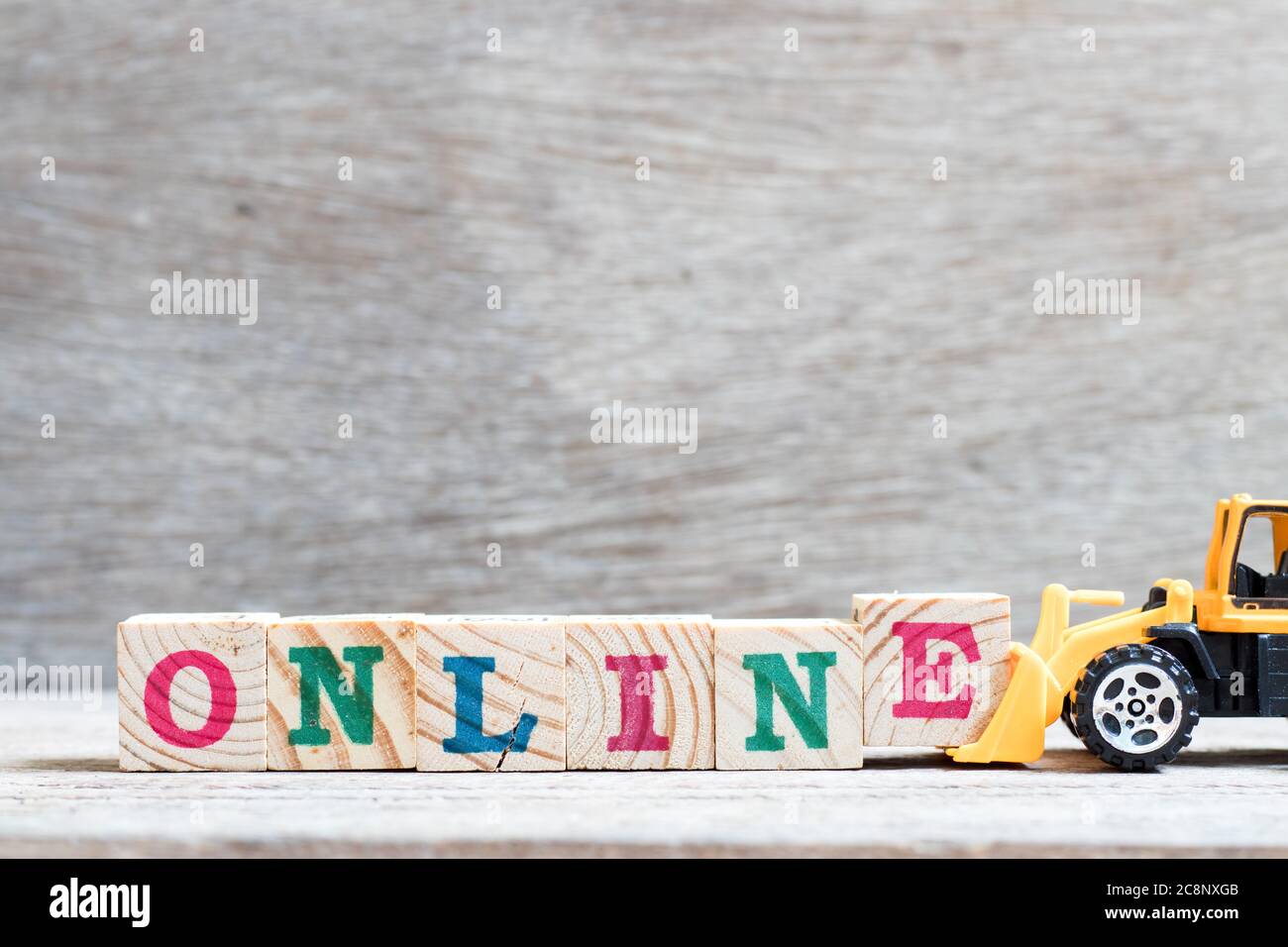 Toy bulldozer hold letter block e to complete word online on wood background Stock Photo