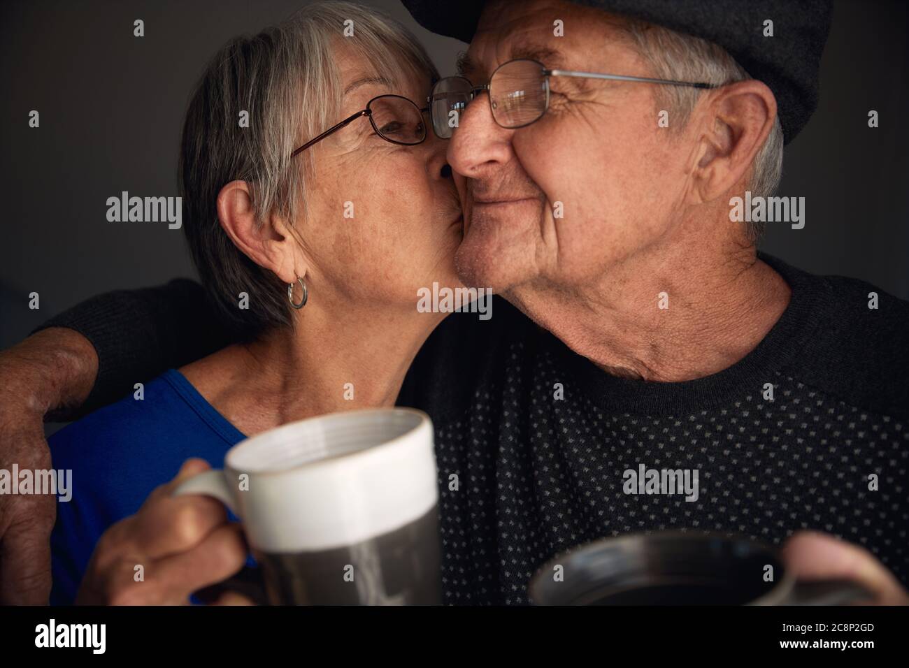 Happy senior couple kissing and laughing whilst drinking coffee. Stock Photo