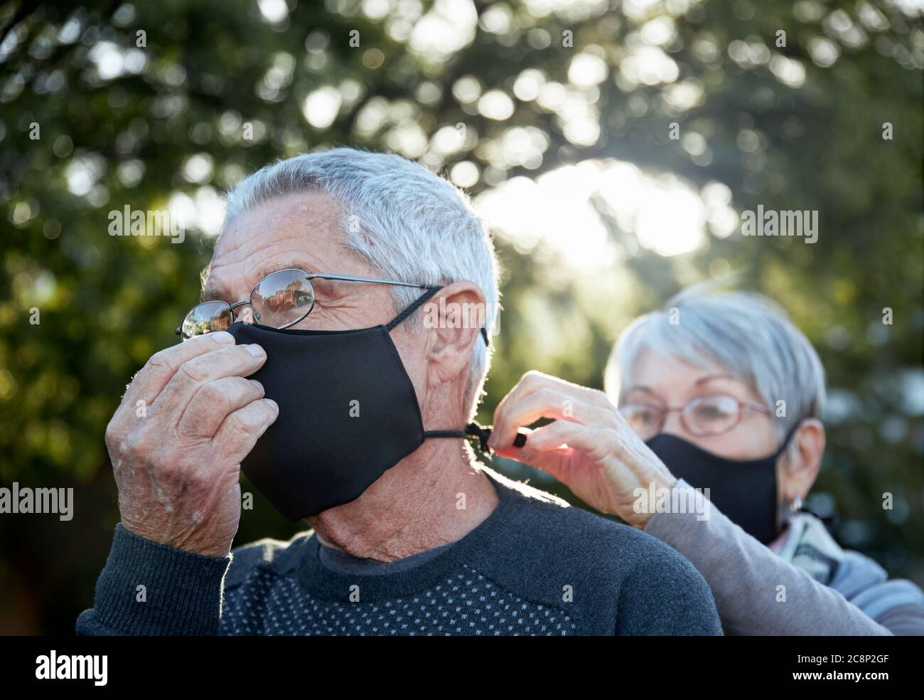 Active senior couple on outdoor walk wearing face masks. Woman helping man with mask. Stock Photo