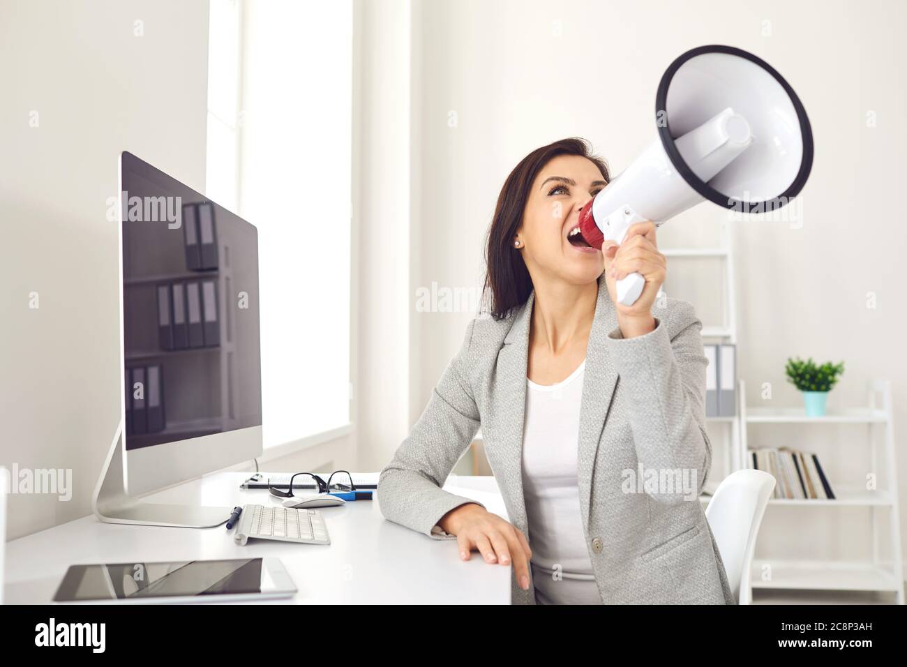 Business Woman with a megaphone in hand shouting while sitting at a table in the office Stock Photo
