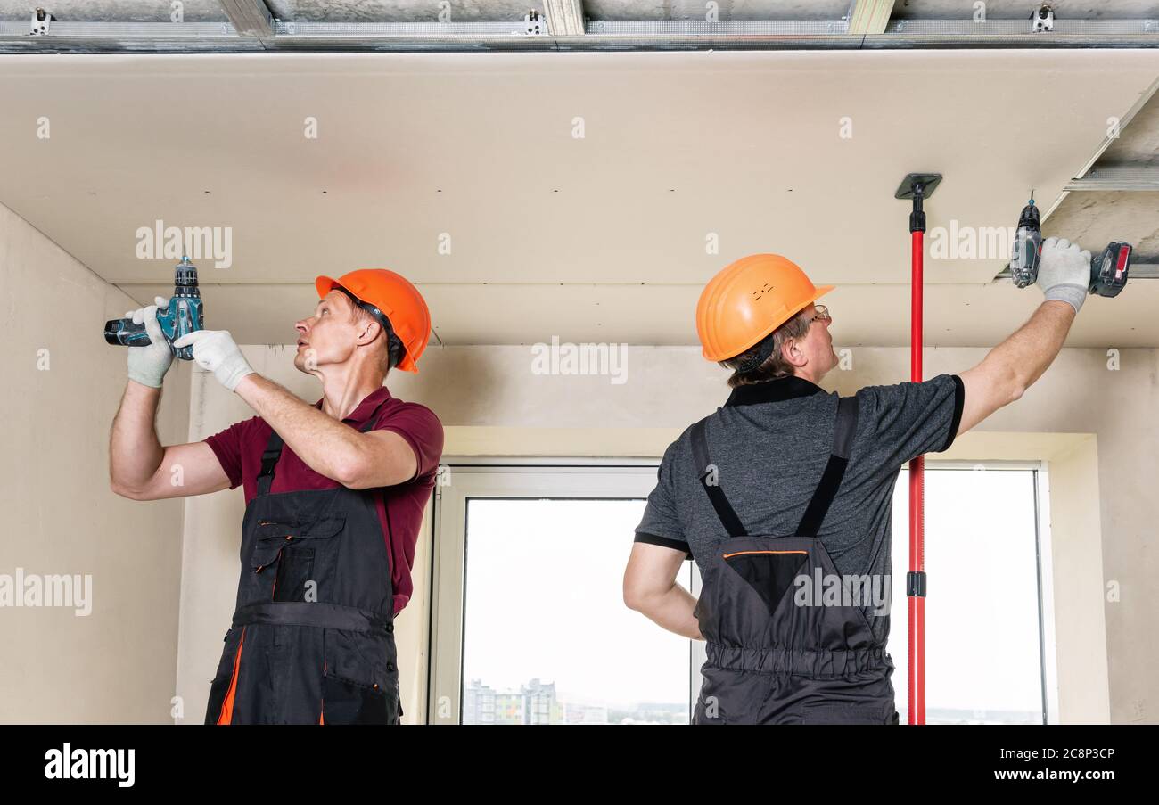 Installation of drywall. Workers are using screws and a screwdriver to