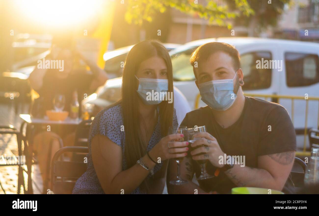 Spain Madrid. Caucasian couple toasting with beer wearing sanitary mask. Reopen pubs and club after quarentine coronavirus Covid-19. Man and woman dri Stock Photo