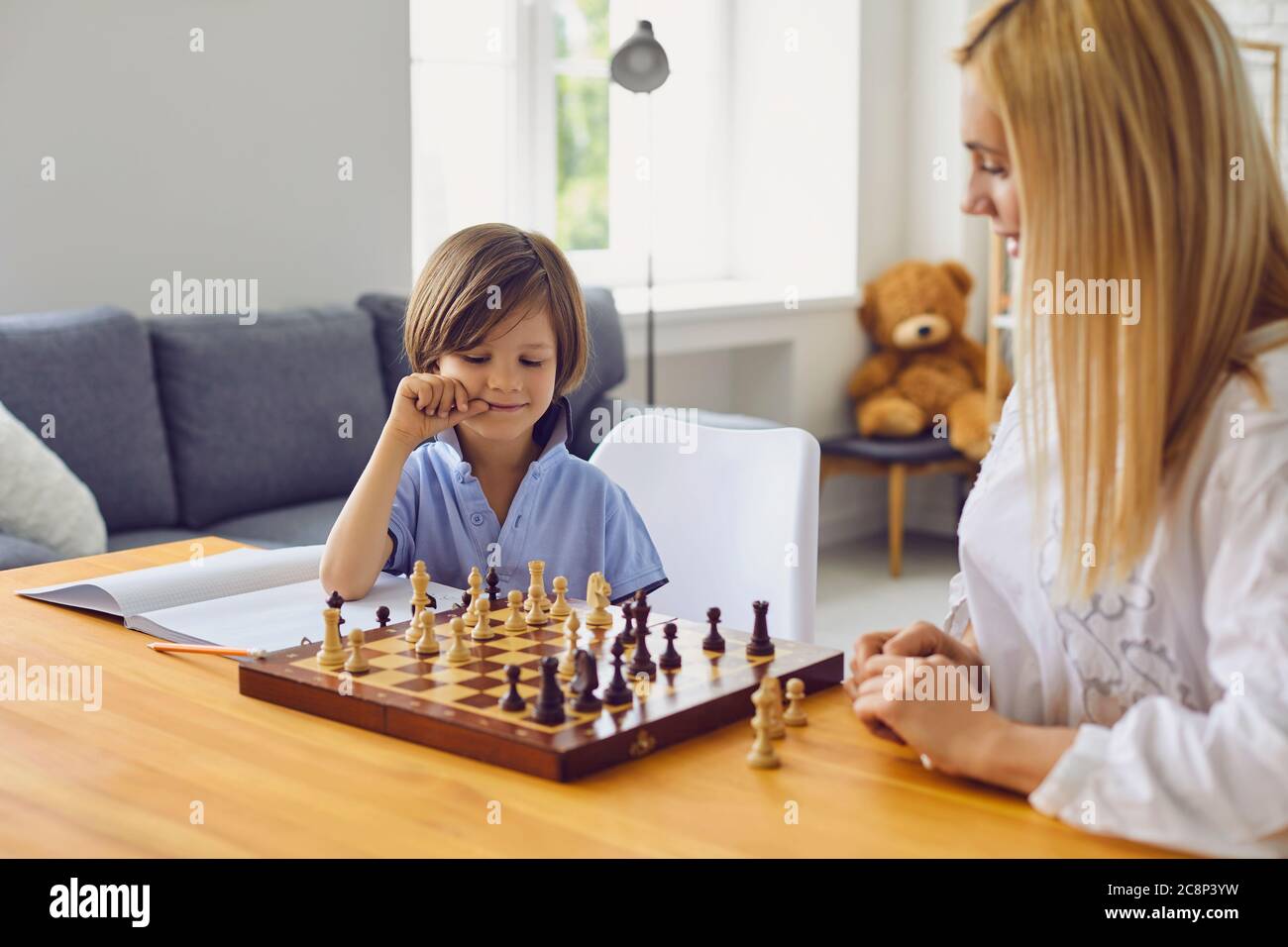 Family hobbies. Young mother playing chess with son at home. Little boy engaged in board game with his parent in room Stock Photo